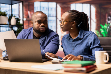 Black man and woman sit at desk analyzing financial documents and tracking expenses, income and...
