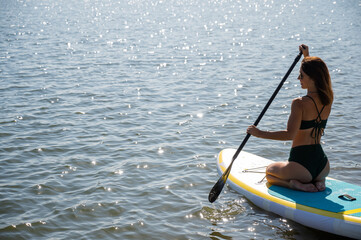 Fototapeta premium Beautiful caucasian woman is swimming on a SUP board.