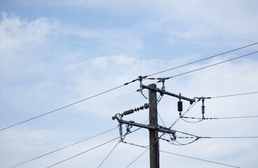 Wooden utility pole with high voltage power lines against blue sky with scattered clouds. Electrical wires crisscross, supported by insulators. Represents energy transmission, infrastructure,