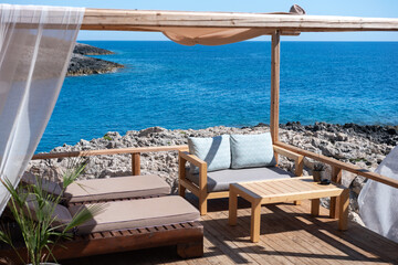 A luxurious and tranquil lounge area with comfortable sunbeds on a wooden deck overlooking the deep blue Ionian Sea in Zakynthos. The perfect image of a luxury travel resort and relaxation.