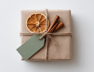 Simple, rustic gift box, wrapped in kraft paper, tied with twine, adorned with dried orange slice and cinnamon sticks.  A muted green tag is attached