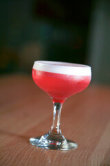 A vibrant red cocktail served in a classic coupe glass, perfectly chilled with a foamy top layer. 