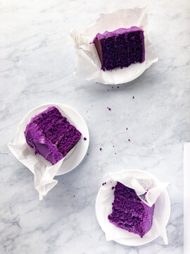 Three rich, purple ube cake slices displayed on white marble, with minimalistic styling and high contrast. Perfect for food blogs, dessert features, or baking-related content.