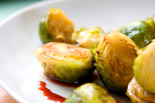 A close-up of roasted Brussels sprouts, halved and glazed, served on a clean white plate. The vibrant greens and caramelized texture highlight a healthy and delicious vegetable side dish.