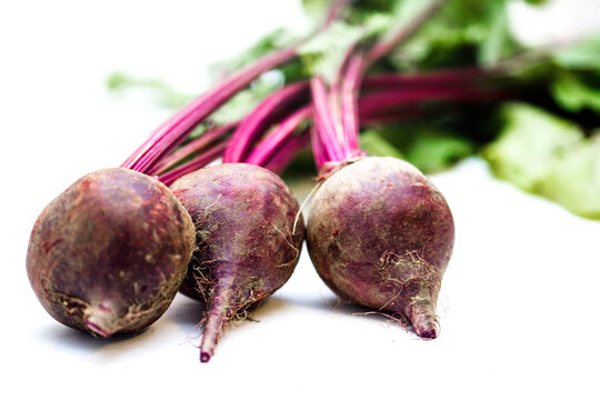 A vibrant bunch of freshly harvested organic beets with roots and leafy stems intact, set against a clean white background. Ideal for promoting farm-to-table food, gardening, or healthy lifestyle them