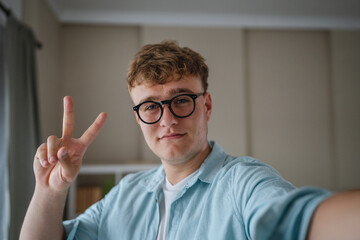 self portrait of young caucasian man make thumbs and smile at home