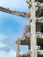 Demolition of a concrete building with machinery on a clear day near an urban area