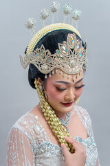 A graceful Indonesian bride in traditional Sundanese attire looks down with a serene smile. Her...