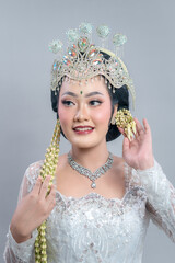 A graceful Indonesian bride in Sundanese traditional attire smiles gently, adorned with a sparkling...