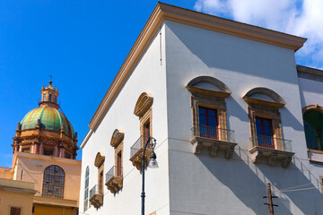Charming street scene in Palermo, with a white building with arched windows and distinctive dome with a green roof and ornate design, likely part of a historic church