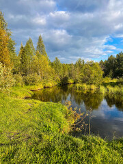  Winding forest river with calm reflective surface and lush green surroundings. Clear summer day with blue sky and scattered clouds.