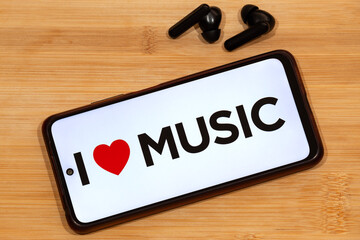 a smartphone with i love music phrase at the screen and a wireless earphones over a wooden...