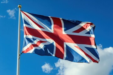 United kingdom flag waving against a bright blue sky with scattered clouds in the background view