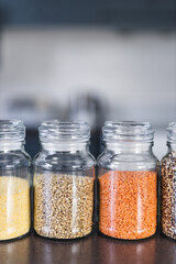 clear pantry jars with different types of grains and legumes including quinoa  lentils buckwheat and barley on benchtop with kitchen bokeh, simple ingredients