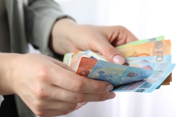 Woman counting euro banknotes indoors, closeup view