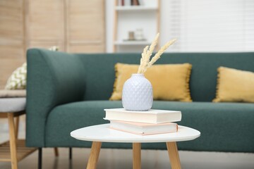 Dried spikes in vase and books on white table indoors
