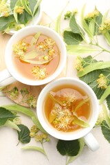 Fresh linden tea in cups and flowers on white table, flat lay