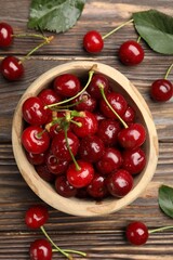 Fresh wet cherries in bowl and leaves on wooden table, flat lay