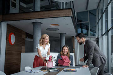 Business team surprising colleague with flowers and gift in modern office