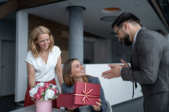 Businessman congratulating businesswoman and giving a gift and flowers