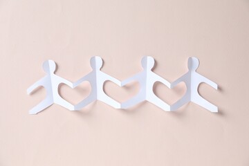 Paper figures of people holding hands on beige background, top view