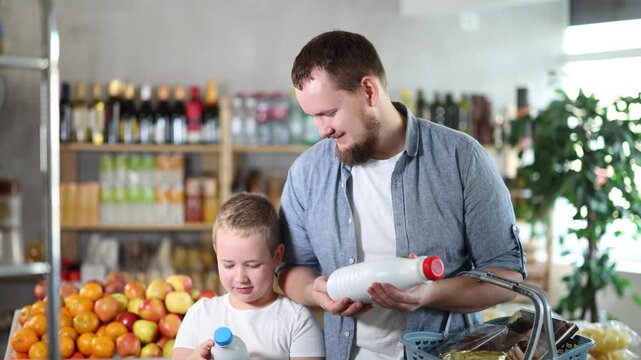 Man with son hold packages bottles and choose consider milk in store. High quality 4k footage