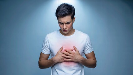A young man in a white t shirt with hands on his chest and a red glow indicating pain or discomfort