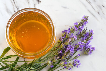 Top down glass jar with honey and lavender flowers on marble surface