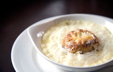 Golden brown cheese soufflé surrounded by a rich, creamy sauce served in an elegant white dish. Perfect for illustrating gourmet recipes, upscale dining, or French cuisine.