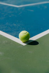 Bright Tennis Ball Resting on Court Corner Where Green and Blue Surfaces Meet Under Direct Sunlight