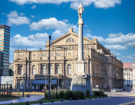Buenos Aires iconic Teatro Colon, an architectural masterpiece, with the imposing General Juan Lavalle Monument in the foreground, under a blue sky with white clouds.