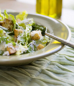 Macro shot of a fresh Caesar salad featuring crisp romaine lettuce, golden croutons, grated parmesan cheese, and creamy dressing. A fork rests in the bowl, ready to eat.
