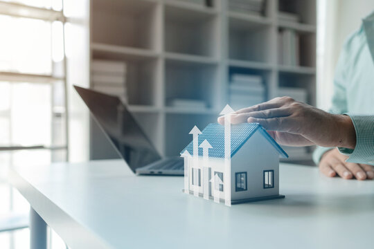 A concept image shows a hand interacting with a model house, symbolizing a rising property market, value appreciation, and growing real estate investment opportunities.