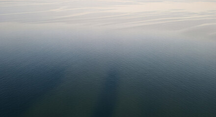 Fototapeta premium Aerial view of calm water with subtle ripples and a gradient from dark blue to light, reflecting the sky above.