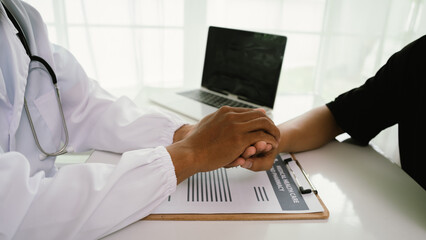 A doctor offers emotional support by holding a patient's hand during a medical consultation,...