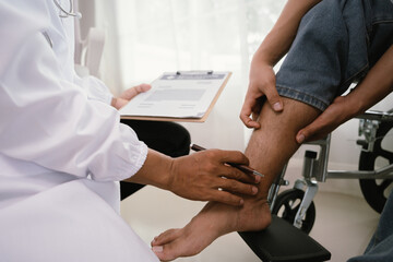 A doctor gently places a hand on a patient's knee, who is seated in a wheelchair, while holding a clipboard, signifying medical consultation and care.