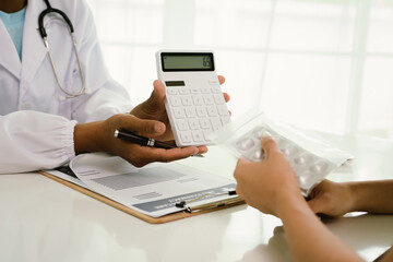 A doctor consults with a patient, explaining medical documents at a desk with a clipboard, laptop,...