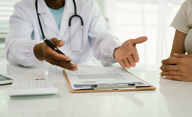 Fototapeta premium A doctor consults with a patient, explaining medical documents at a desk with a clipboard, laptop, and calculator, emphasizing care, professionalism, and clear communication.