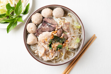Thai noodles soup with sliced pork, minced pork, meatball and liver in a bowl eating with fresh vegetables on white background, Traditional Thai street food, Top view