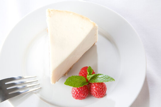 Elegant slice of creamy cheesecake served with fresh raspberries and a mint garnish on a white plate.