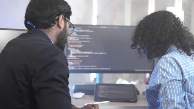 A senior Indian developer mentoring a colleague, pointing at code during a collaborative pair programming session. Concept for teamwork, knowledge transfer, and agile development.