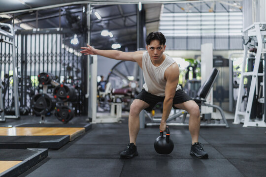 Determined asian athlete lifting kettlebell in modern fitness center