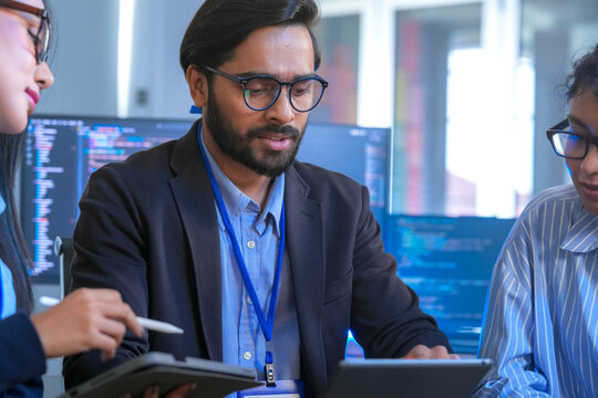 Diverse team of software engineers and data scientists collaborating on a project, using tablets and analyzing code. Concept for AI development, cybersecurity, and tech innovation.