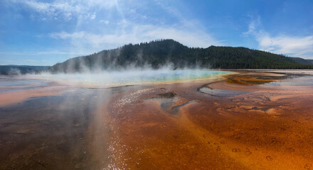 Panoramic shot of a vast geothermal area, vibrant colors, rising steam under a bright blue sky.