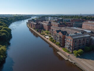 Obraz premium Aerial view of a river flowing through a city, with brick buildings lining the waterfront and lush greenery on the opposite bank under a clear sky