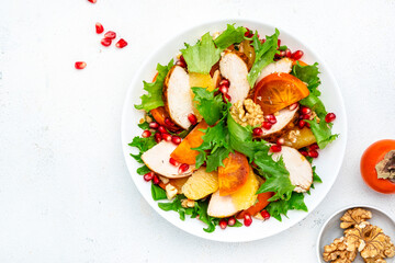 Yummy persimmon salad with grilled chicken, pomegranate, walnuts, oranges and lettuce, top view