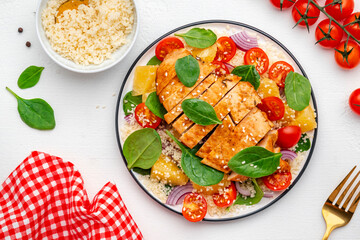 Yummy salad with chicken, couscous, tomatoes, onion, spinach and orange. White table background, top view