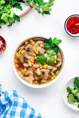 Mexican style chicken soup with mushrooms, corn, white beans, hot chili and cilantro. Black table background, top view