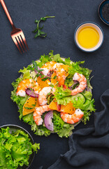 Juicy shrimp salad with orange, lettuce, red onion with olive oil and juice dressing, black background, top view