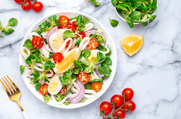 Gourmet seafood salad with squid, juicy orange, red tomatoes, lamb lettuce on marble table, top view